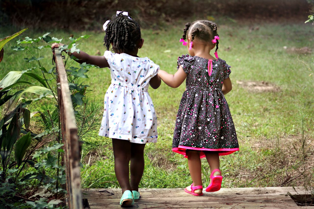 about-02 Two young girls in colorful dresses walking hand in hand outdoors, embodying friendship and innocence.