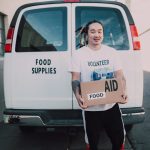 About Volunteer holding food aid box in front of a van for community service donation.