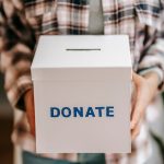 About Close-up of a person holding a donate box, encouraging charity and support.