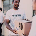 About A volunteer hands a box labeled aid and food during an outdoor charity event.