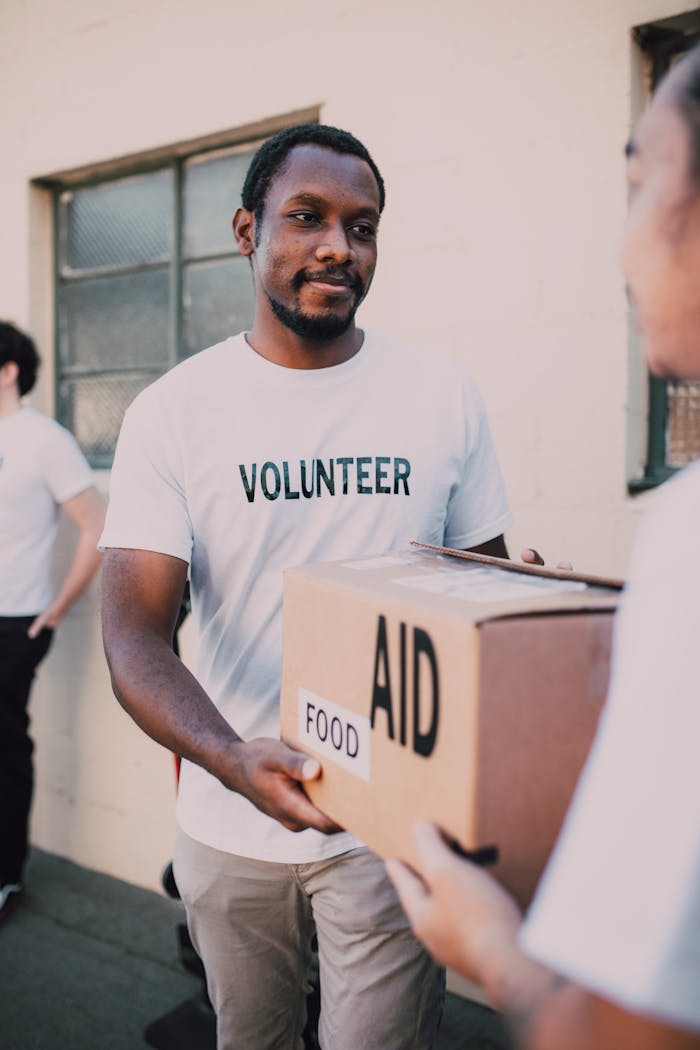 A volunteer hands a box labeled aid and food during an outdoor charity event.