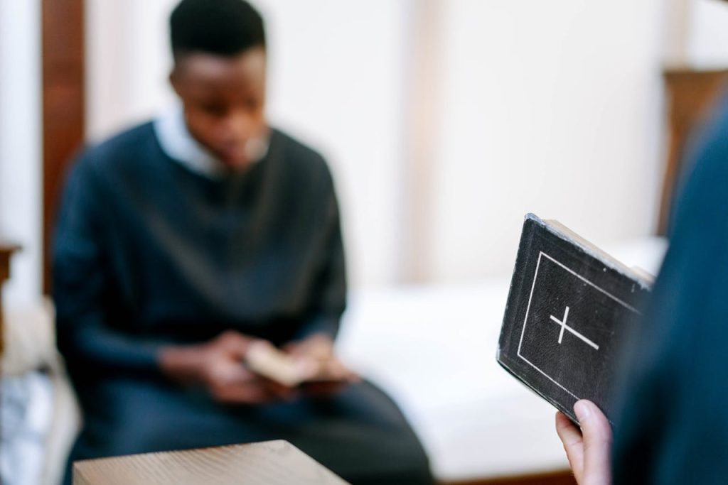shallow-focus-photo-of-a-bible-held-by-a-person-8955280 A person in religious attire reads a Bible indoors, focusing on faith and reflection.