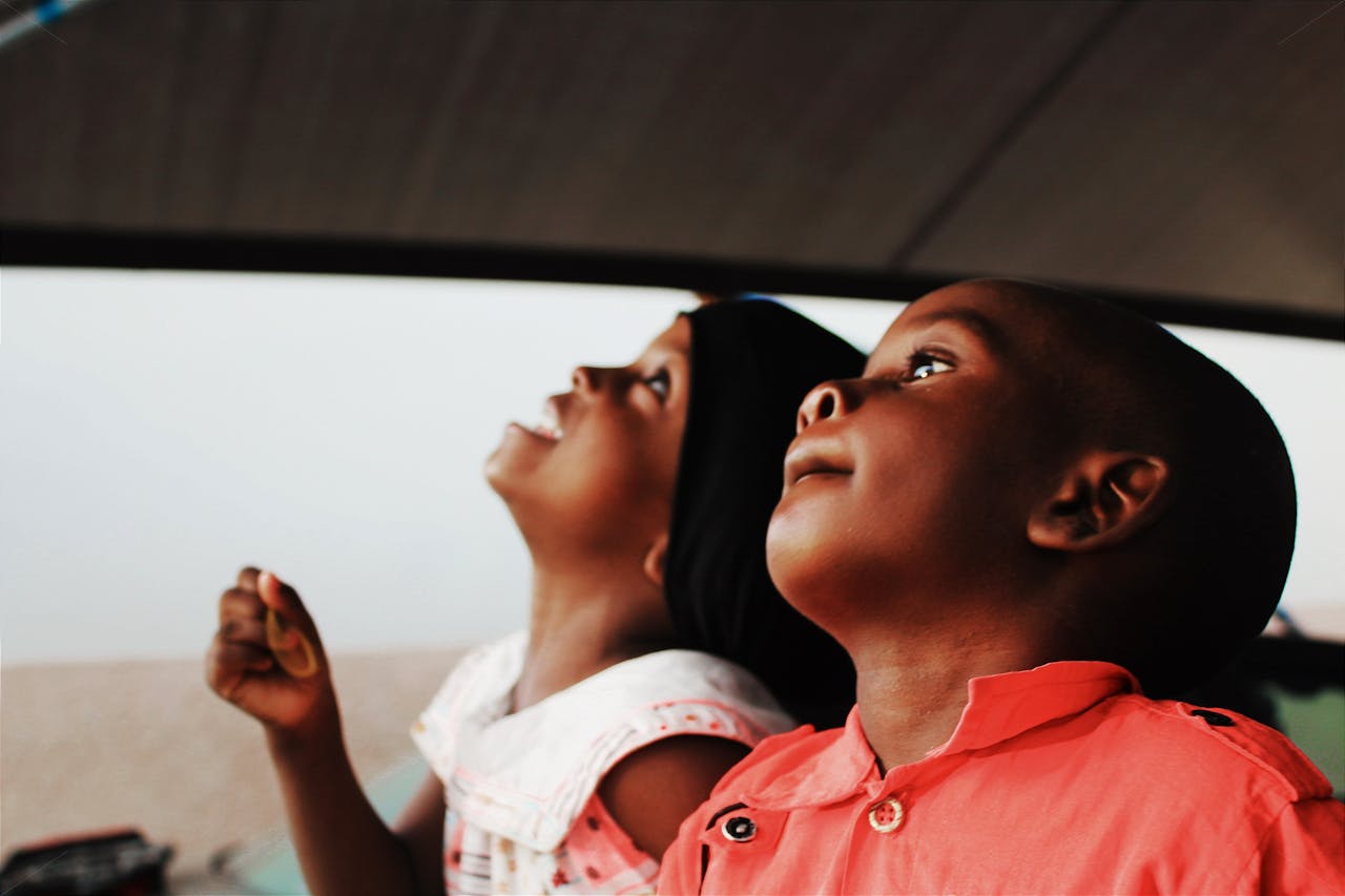 hero-about Two joyful African children look upwards with anticipation, capturing a moment of wonder and curiosity.